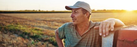 EWE business Fahrplanoptimierung Ein Landwirt, der an einem Trecker lehnt, im Hintergrund ein Feld