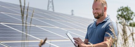 Die EWE business App für Ihre Direktvermarktung Ein Mann prüft etwas auf seinem Smartphone, daneben PV-Module