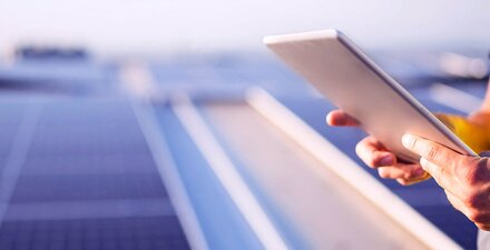 Laden Sie sich jetzt das Whitepaper herunter! Ein Mann, der auf einer PV-Fläche ein Tablet bedient