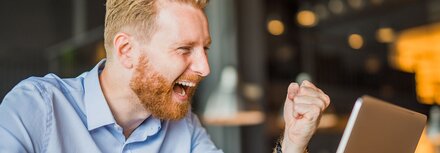 Junger Mann freut sich über einen erfogreichen Abschluss, den er mit seinem Notebook durchgeführt hat - Stock-Fotografie