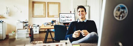Ein Mann an einem Schreibtisch zurückgelehnt im Stuhl und lachend