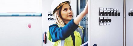 Flexibilitätsvermarktung für Kraftwerke Frau mit Helm vor Schaltschrank