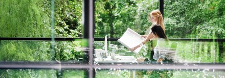 Korridorphase CO2-Preis Zwei Kolleginnen bei der Büroarbeit vor einer Fensterfront, hinter der Bäume zu sehen sind.
