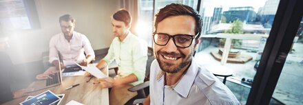 EWE business Gas fix Ein Mann mit Brille an einem Bürotisch, im Hintergrund zwei Kollegen