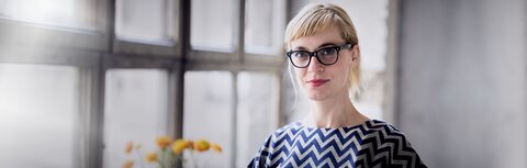 Entwicklung der Energiepreise Eine Frau mit Brille guckt in die Kamera, dahinter eine Fensterfront