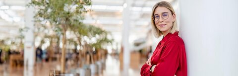 Digitaler Stromzähler Eine junge Frau mit Brille, die sich an eine Wand anlehnt und lächelt