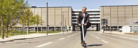 EWE business Strom für Unternehmen Ein Mann im Anzug auf einem E-Roller vor einem Industriegebäude