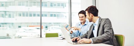 Zwei Männer an einem Arbeitsplatz mit einem Laptop, die ein Diagramm ansehen