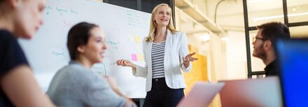 Beratung zu grünen Lösungen Eine blonde Frau erläutern einer Gruppe etwas vor einem Whiteboard.