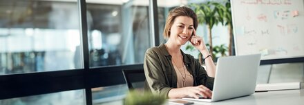 EWE business Webinar "Klimaneutrales Unternehmen" Eine Frau am Schreibtisch, die interessiert auf Ihren Arbeitsrechner guckt