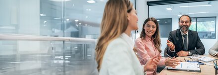 Zwei Frauen und ein Mann unterhalten sich geschäftlich an einem Tisch.