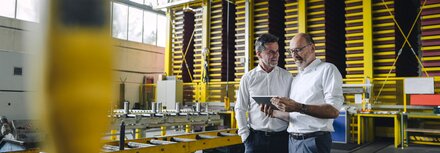 Energieberatung für KMU und Selbstständige Zwei Männer in weißen Hemden unterhalten sich und gucken auf ein Tablet in einer Betriebswerkstatt.