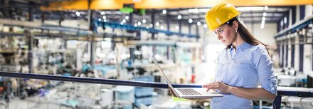 EWE Leased Line Frau mit Helm in Fabrikhalle schaut auf Laptop