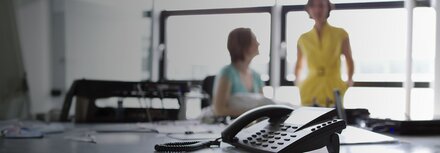 Fraud-TK-Anlagen von EWE Festnetztelefon im Vordergrund, zwei Frauen unscharf im Hintergrund