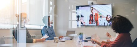 Mehrerer Menschen im Konferenzraum schauen auf einen Bildschirm während einer Videokonferenz