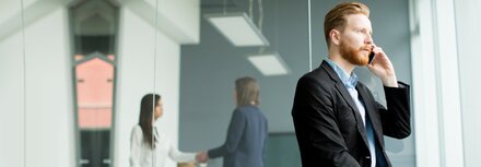 EWE CEO-Fraud Rothaariger Mann telefonierend am Smartphone in einer Büro-Umgebung