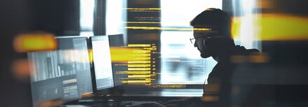 Ein Mann arbeitet in einem abgeschatteten Büro an einem Computer.