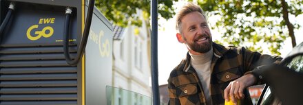 Ein Mann in Flanelljacke lädt sein Auto an einer EWE-Go-Säule