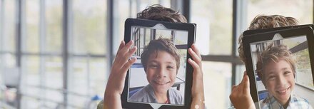Geräte-Wirrwarr an der Schule Kindergesichter auf Tablets, die die Kinder hochhalten