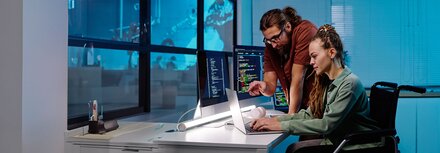 Ein Mann und eine Frau im Rollstuhl vor einem Arbeitsrechner