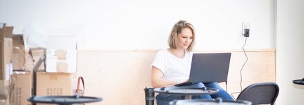 Glasfaseranschluss für Unternehmen Eine Unternehmerin, die mit Laptop in einem Geschäftsraum sitzt, der gerade umgebaut wird