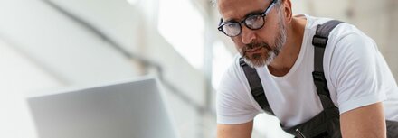 Ein Handwerker mit Latzhose, der etwas in einen Computer eingibt