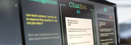 Bildschirme in einem Büro, auf einem wird eine Chatbot-Maske angezeigt.