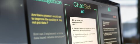 KI - was ist das? Bildschirme in einem Büro, auf einem wird eine Chatbot-Maske angezeigt.