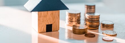 Staatliche Förderung für die Digitalisierung Ihres Unternehmens Ein Haus aus Bauklötzen auf einer Glastischplatte, daneben Münzen