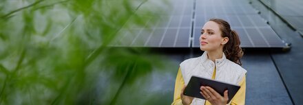 Investitionsbooster: Steuervorteile für neue PV-Anlagen Eine Frau mit Tablet steht vor einer PV-Anlage und lächelt.