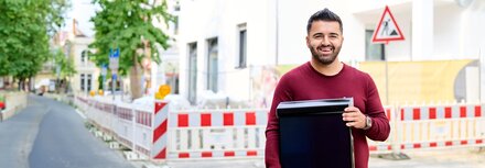 Ismet Kolcu, Fachberater PV und Stromspeicher bei EWE, vor einer Baustelle mit PV-Modul in den Händen