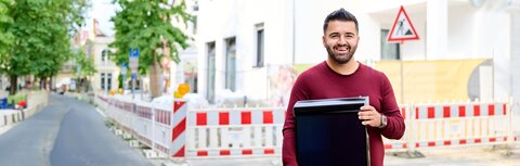 Interview mit Ismet Kolcu, Fachberater PV und Stromspeicher bei EWE Ismet Kolcu, Fachberater PV und Stromspeicher bei EWE, vor einer Baustelle mit PV-Modul in den Händen