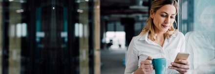 IT-Sicherheit: Was bedeutet was? Eine Frau lehnt an einer Glasfassade und guckt auf ihr Smartphone