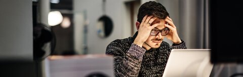 IT-Basisschutz Ein Mann sitzt im Büro vor einem Laptop und grübelt über einen erfolgreichen Cyberangriff auf seinen Arbeitgeber nach.