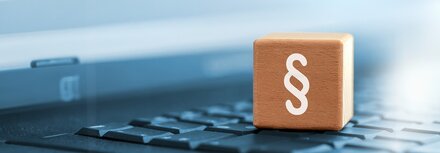 Welche Unternehmen betrifft NIS2? Ein Paragraphen-Zeichen auf einem Holzwürfel, der auf einer Tastatur steht