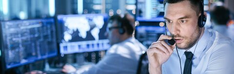 EWE business SOC-as-a-Service Ein Mann spricht in einem blau erleuchteten Kontrollraum in ein Headset