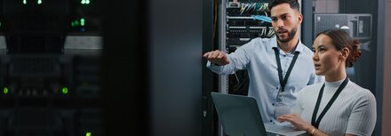 Jetzt vor Zero Day Exploits schützen! Ein Mann und eine Frau mit Laptop, die in einem Serverraum etwas überprüfen