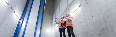 Notlösung für die Beleuchtung: Retrofit Zwei Kollegen mit Schutzhelmen und Sicherheitswesten bei der Neukonzeption der Beleuchtungstechnik auf einer Baustelle