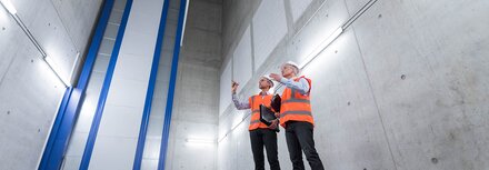 Zwei Kollegen mit Schutzhelmen und Sicherheitswesten bei der Neukonzeption der Beleuchtungstechnik auf einer Baustelle