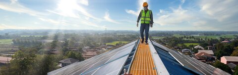 Ratgeber: grüne Energie Ein Wartungstechniker läuft auf einem Fabrikdach, auf dem PV-Module installiert sind