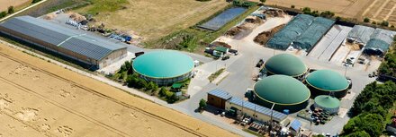 Das Virtuelle Kraftwerk einfach erklärt Eine Luftbildaufnahme einer Biogasanlage, die von landwirtschaftlicher Fläche umgeben ist