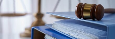 Ein blauer Ordner, darüber ein Richterhammer, daneben eine Waage als Symbol für die Jusitz
