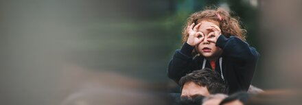 Kleines Mädchen auf den Schultern ihres Vaters blickt suchend um sich.