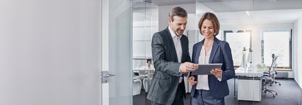 Eine Frau und ein Mann gucken in einem Büro auf ein Tablet.