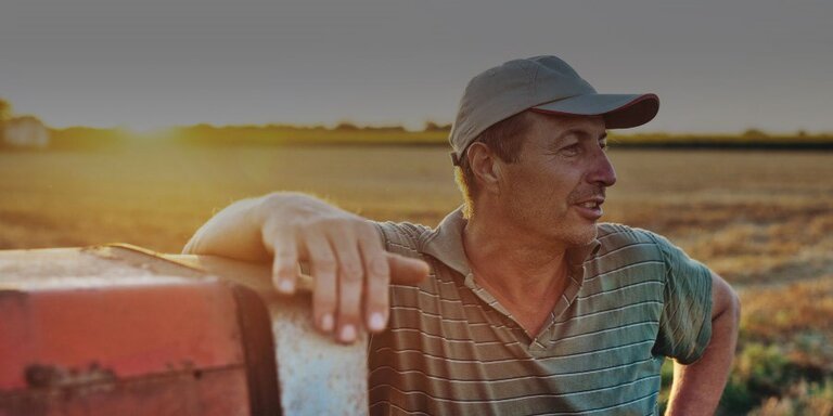 Ein innovativer Landwirt, der an einer Landmaschine auf dem Feld vor dem Sonnenuntergang lehnt.