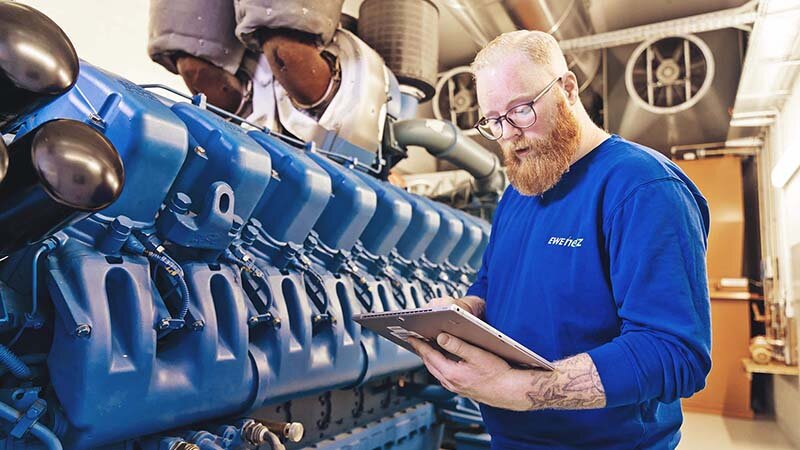 Ein Techniker mit Tablet vor einem blauen Kraftwerk