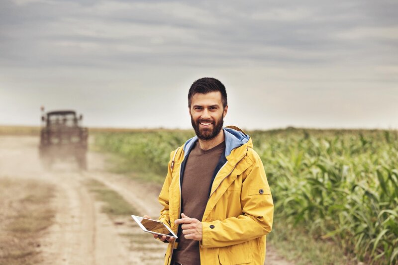 Mann mit Tablet vor Maisfeld und Traktor