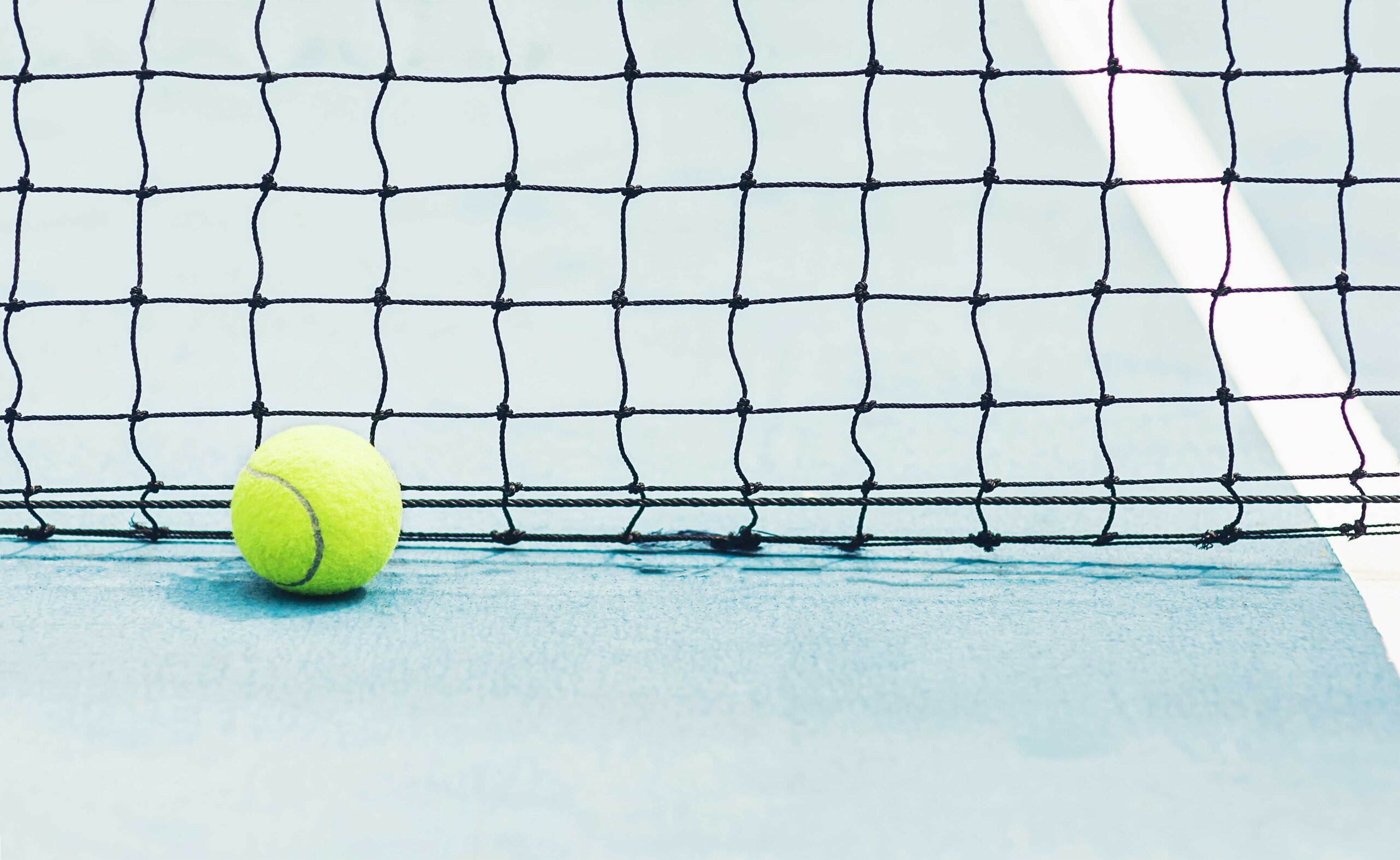 Bild eines Tennisnetzes mit davor liegendem Tennisball