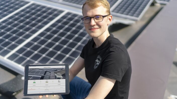 Ein junger Mann mit Tablet sitzt vor der PV-Anlage auf dem Dach bei Müller & Egerer