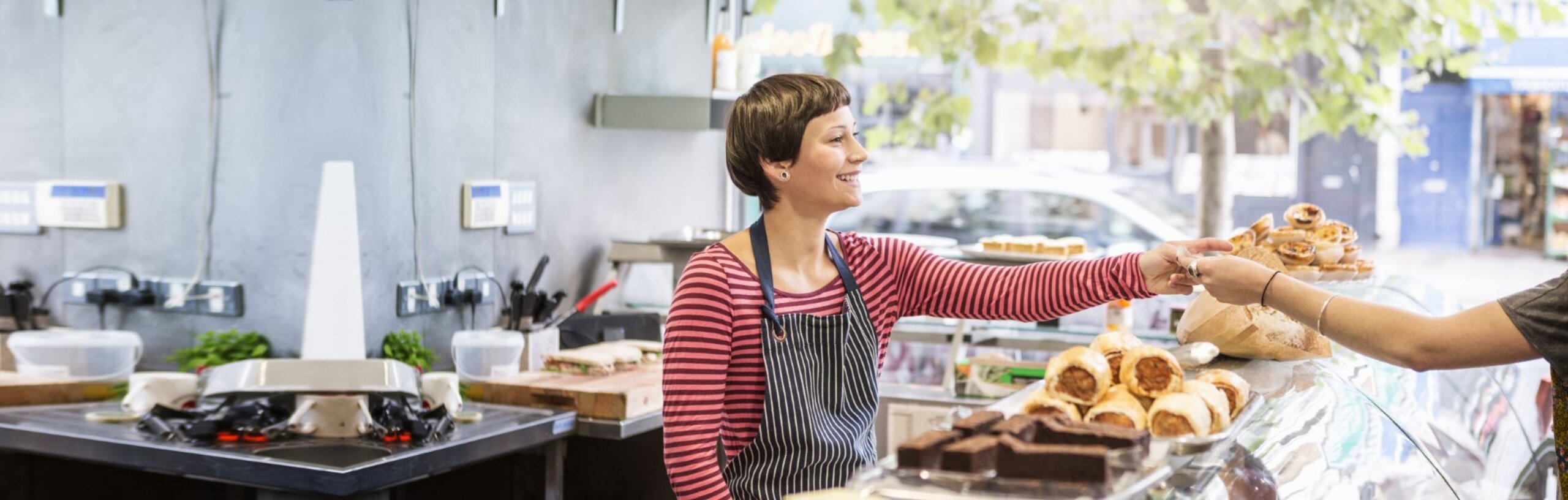 Eine Mitarbeiterin einer Bäckerei nimmt über die Ladentheke Geld von einem Kunden an.